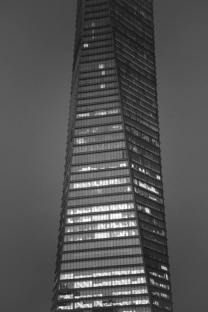 Black and white photo of an illuminated skyscraper with a modern glass facade, standing tall at night.
