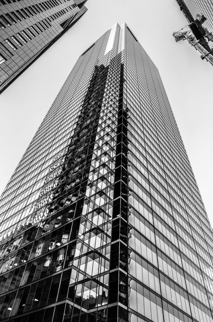 Low angle black and white view of a modern skyscraper with reflective glass facade and surrounding buildings.